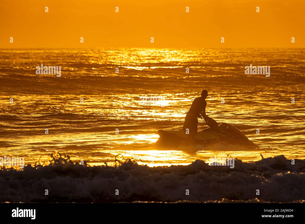 Silueta de joven montando una moto de agua y mirando hacia el amanecer en el horizonte de una playa hermosa Foto de stock