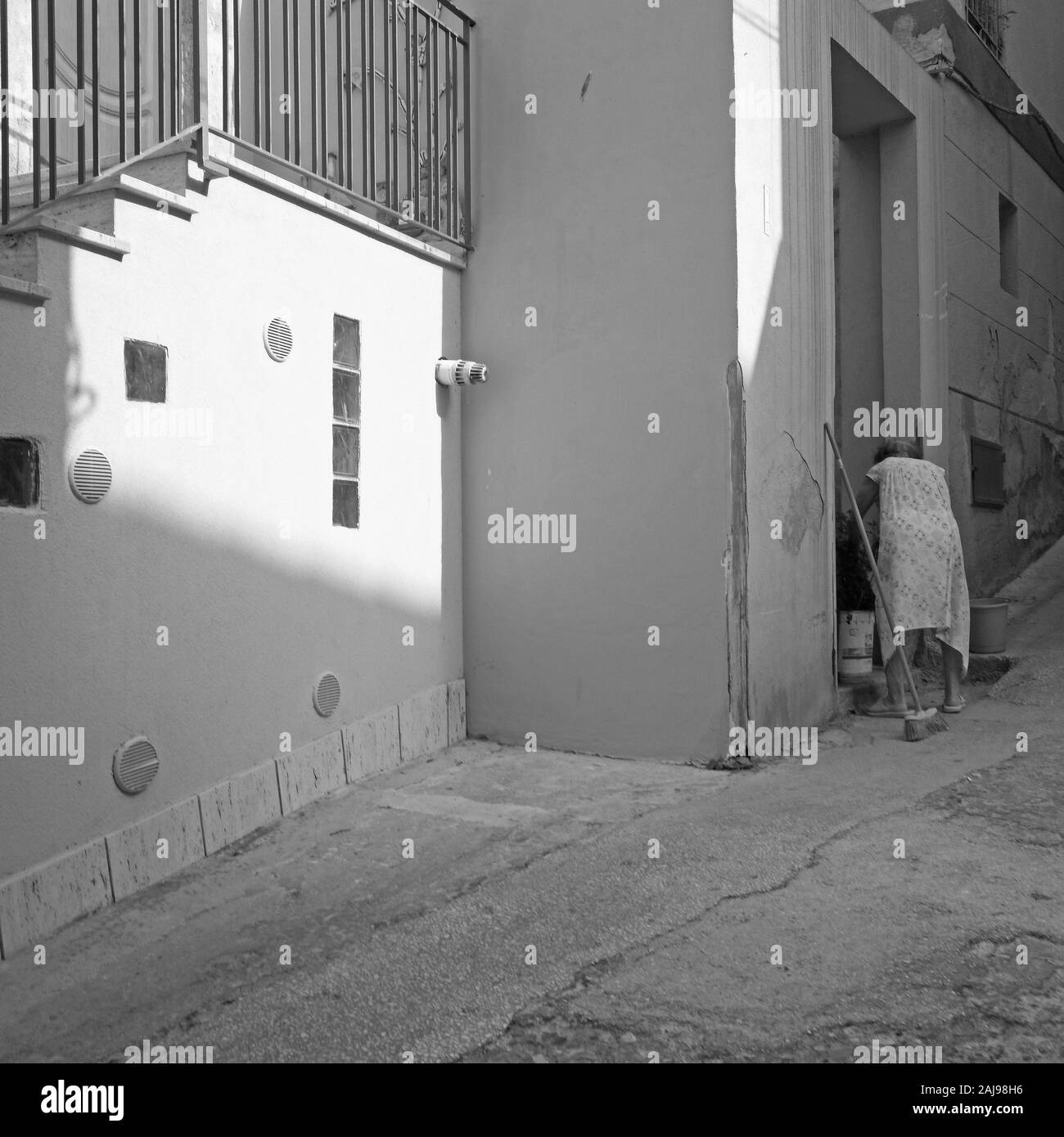 Anciana la limpieza fuera de su casa en una tranquila calle residencial en el distrito histórico de Sciacca, Sicilia, Foto de stock