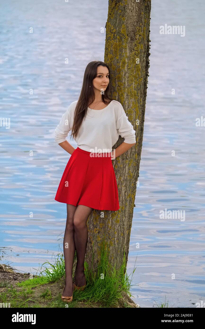 Retrato de una chica en falda roja y blusa blanca ha impactado contra un  árbol en la ribera del río Fotografía de stock - Alamy