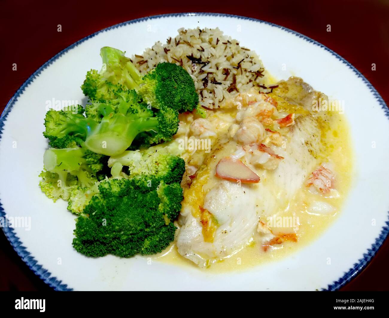 Cena de Marisco saludable con un lomo de bacalao, coronado con cangrejo y una salsa de mantequilla de ajo limón, arroz pilaf y brócoli cocido Foto de stock