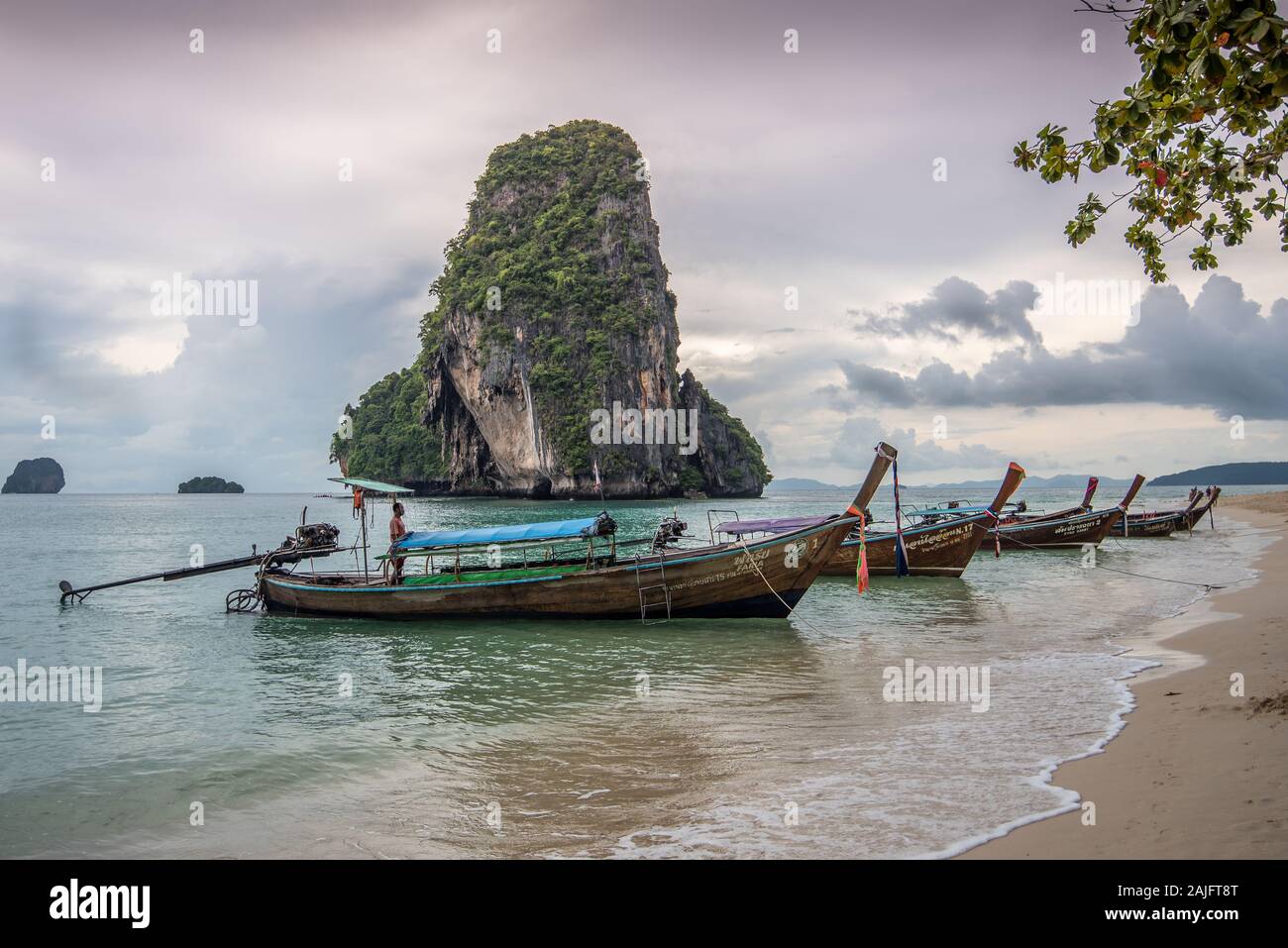 Playa Phra nang, Krabi, Tailandia: Barcos de cola larga, barcos de madera tailandeses tradicionales, el hombre tailandés y ko sonaron isla nok contra un nublado dramático Foto de stock