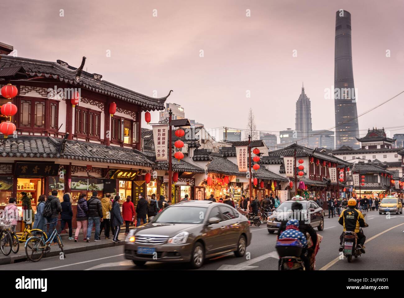 Shanghai, China: Escena callejera en el casco antiguo con edificios asiáticos tradicionales, gente coches de tráfico motos y rascacielos Shanghai Tower Foto de stock