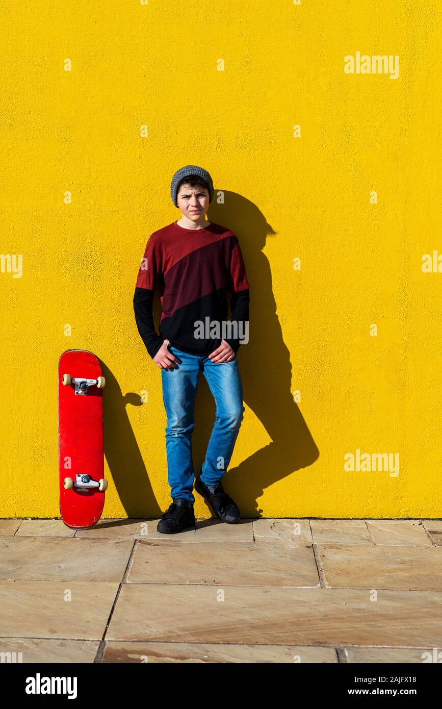 Adolescente con tapón de lana apoyado contra una pared amarilla mientras busca cámara Foto de stock