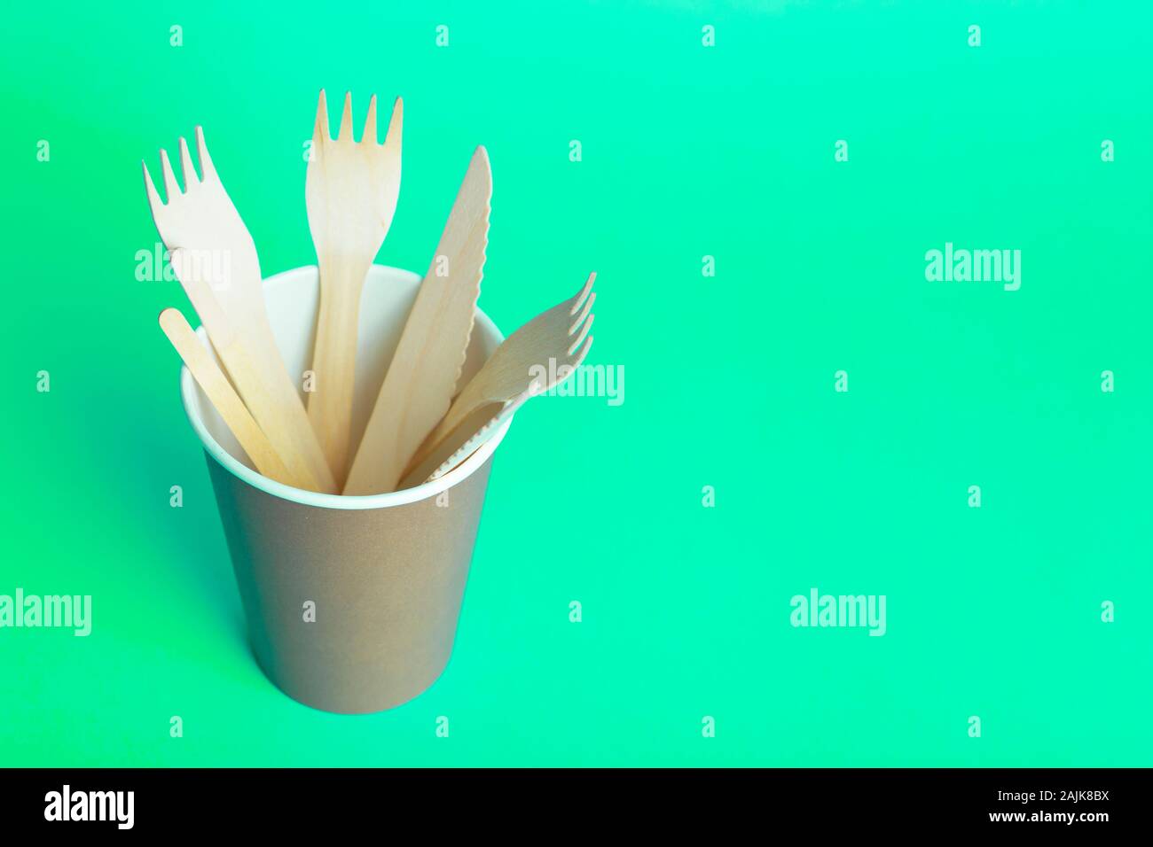 Horquillas de madera, cucharas y cuchillos para la comida en un vaso de papel sobre un fondo coloreado. Eco-friendly vajilla desechable sin plástico. Foto de stock