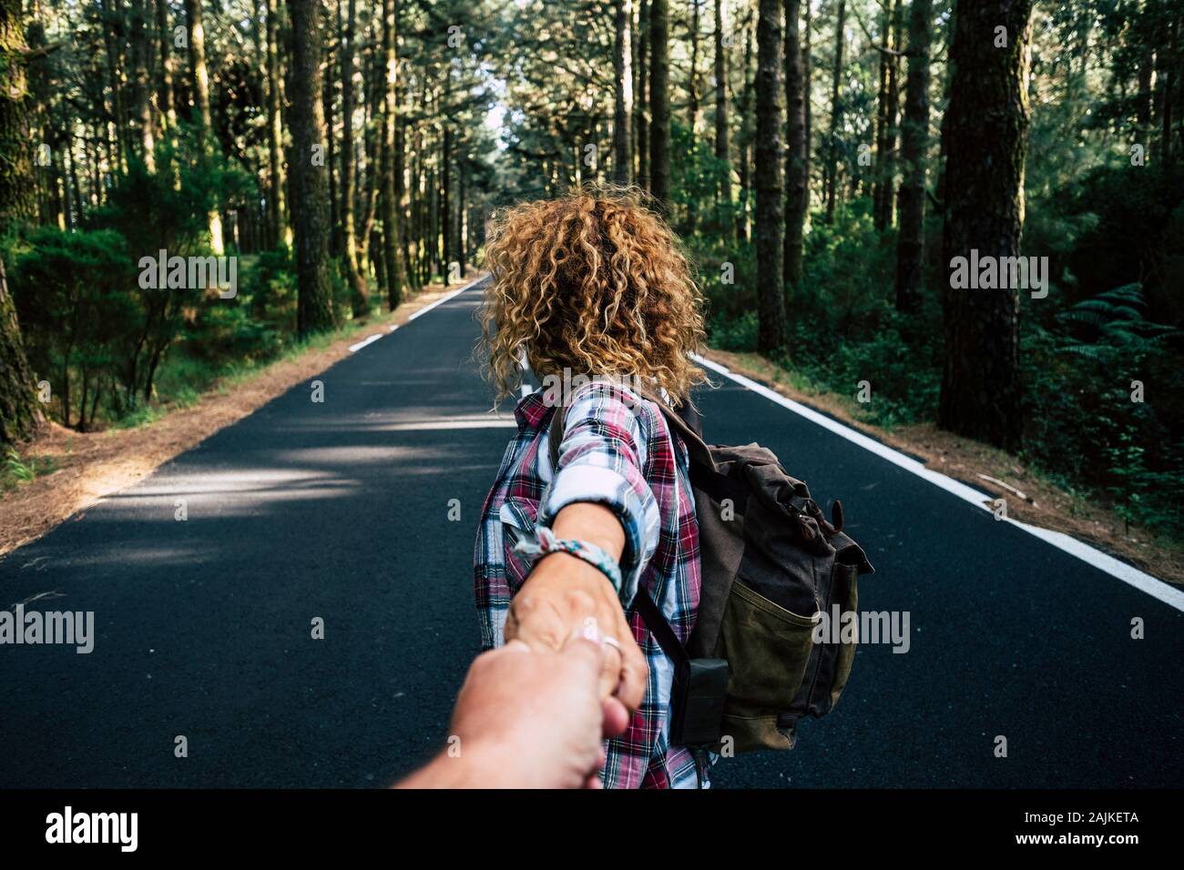 Par viajar juntos caminando con mochila de un bosque en una larga carretera de asfalto - el hombre punto de vista - Manos con amor y relaciones - alte Foto de stock