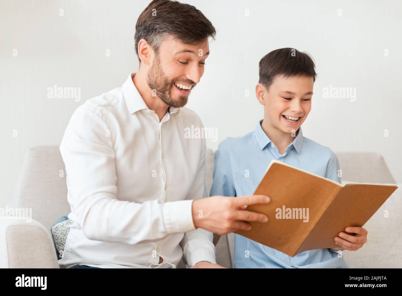 Padre e Hijo Feliz lectura y riendo sentados juntos en el sofá en casa