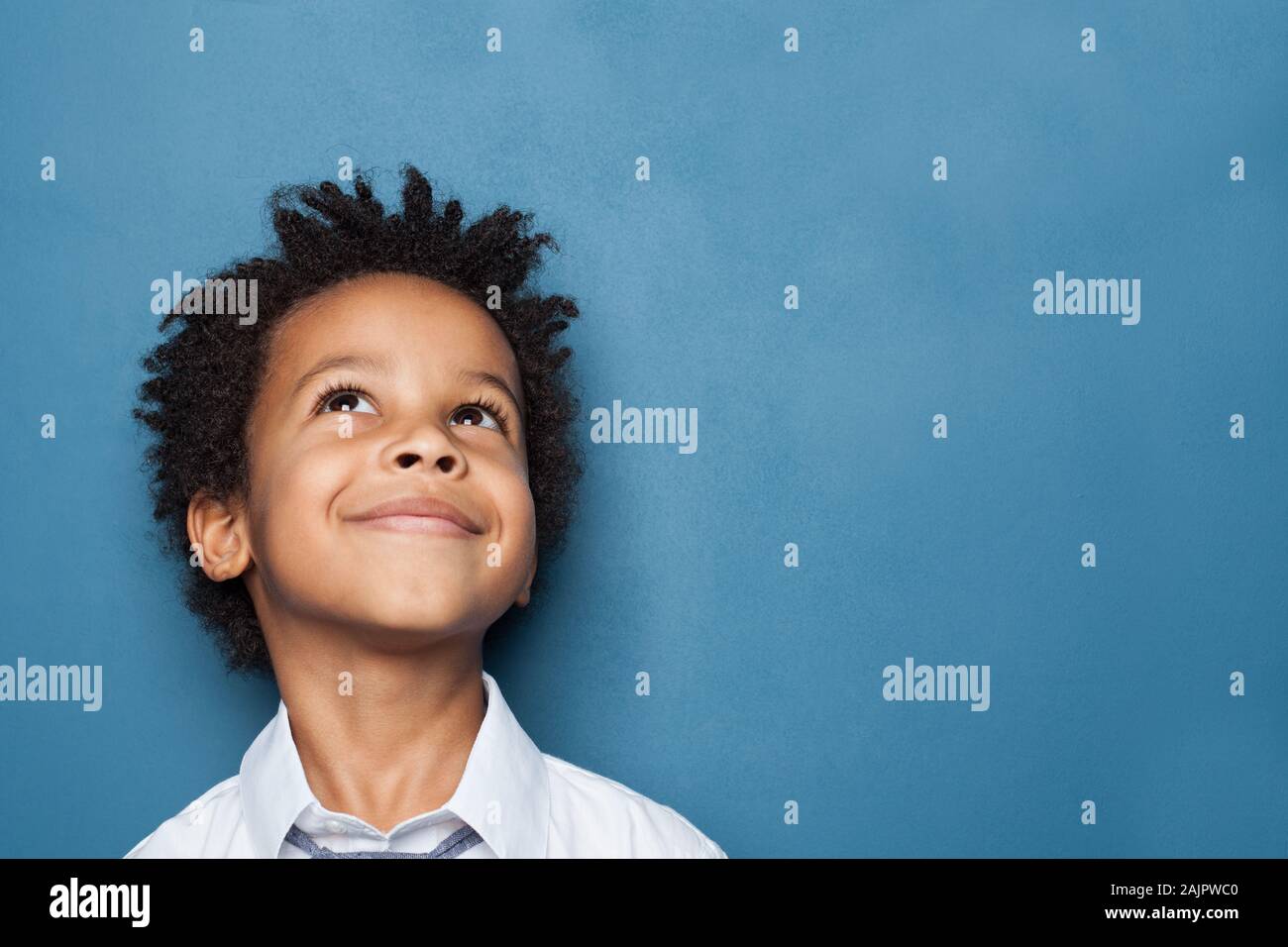 Pequeño niño negro Niño sonriendo y mirando hacia arriba sobre fondo azul. Foto de stock