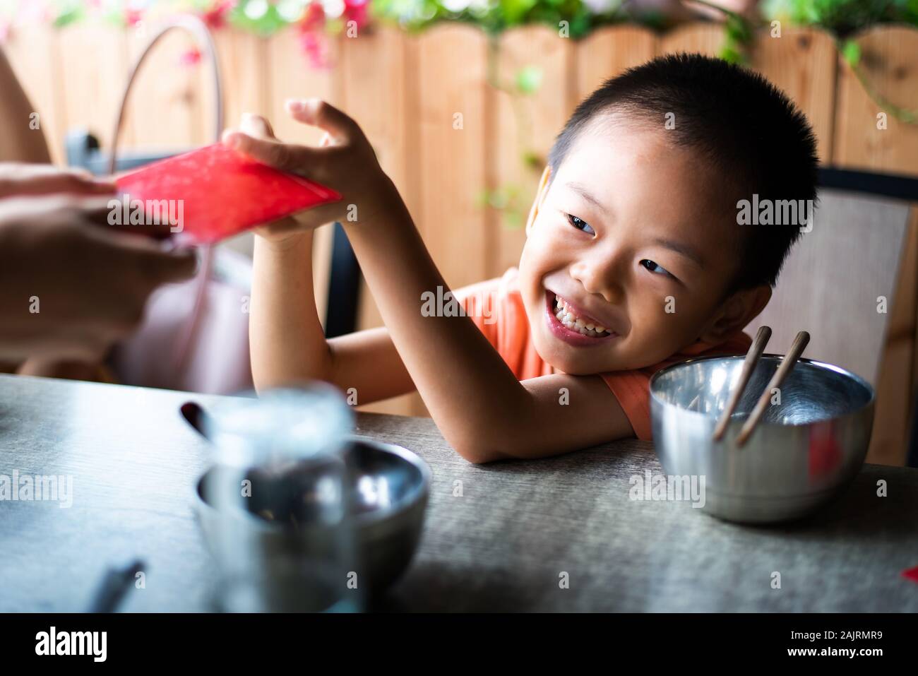 Niño chino recibe de bolsillo rojo sobre la mesa de comedor Foto de stock