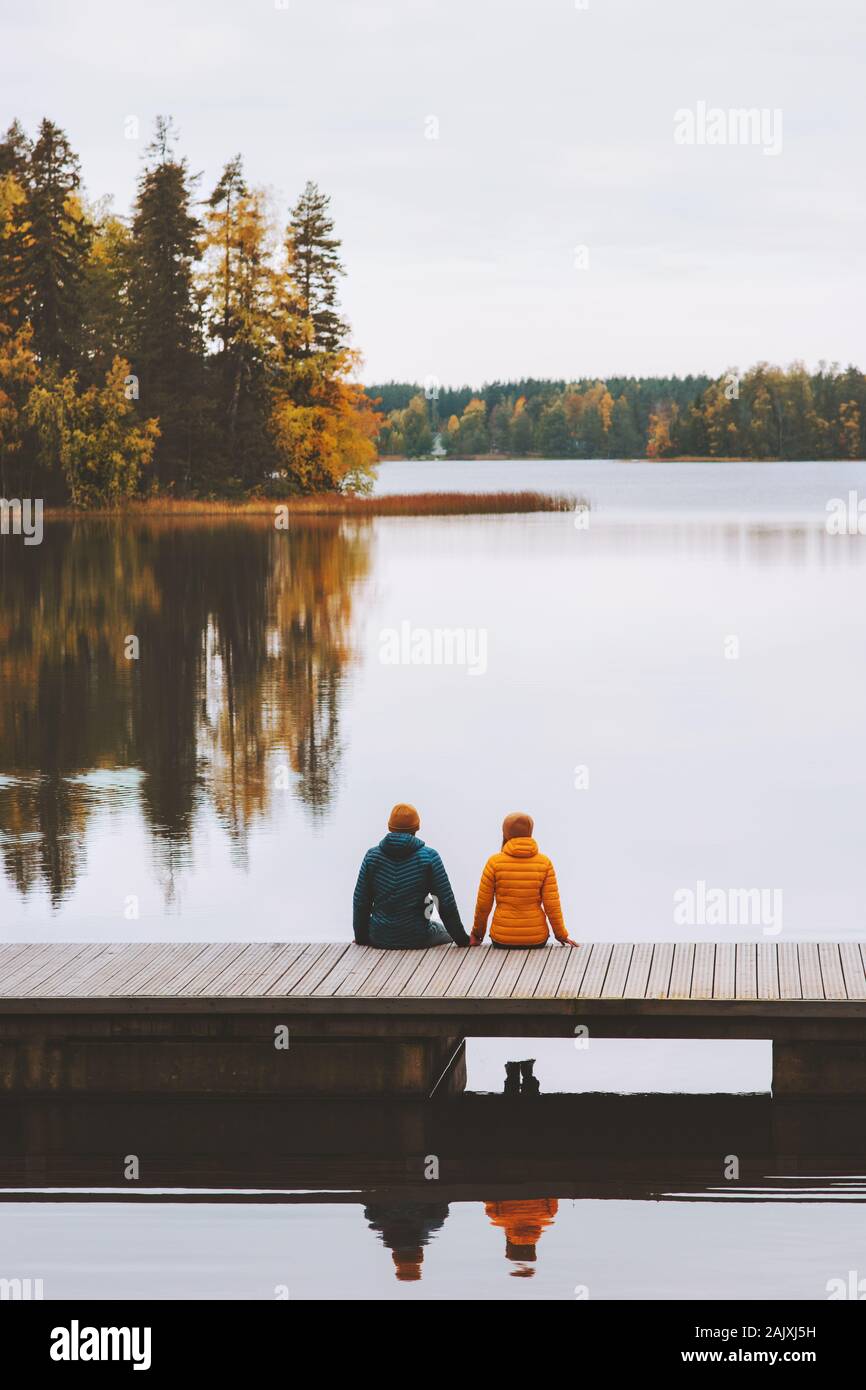 Par viajar en Finlandia la vida familiar relación de amor al hombre y a la mujer amigos sentado en el muelle exterior y lago paisaje forestal temporada de otoño Foto de stock