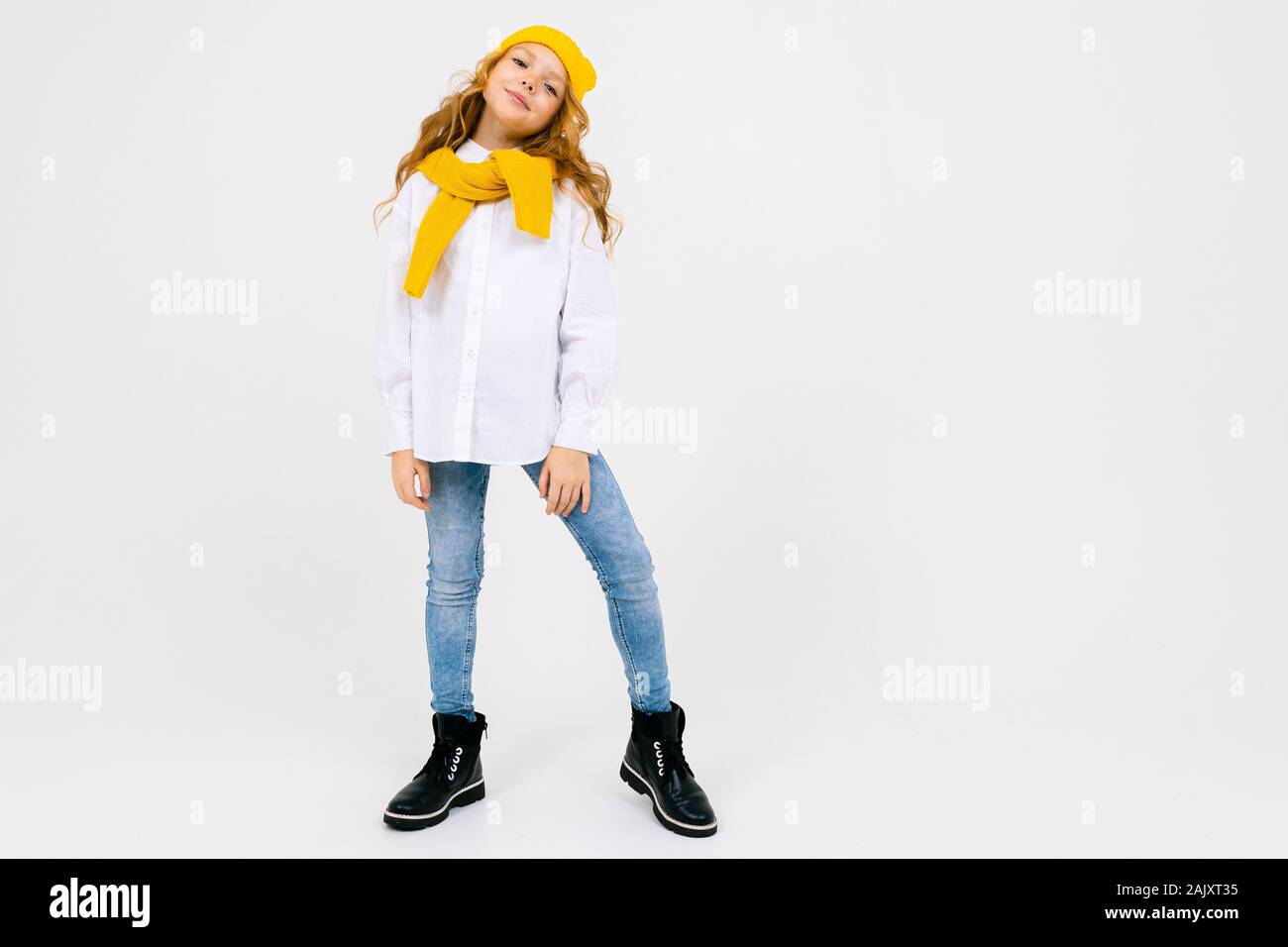 Elegante y atractiva chica caucásica soñando en una camisa blanca y  pantalones de mezclilla y un sombrero amarillo con botas posando con una  pierna levantada sobre un fondo blanco Fotografía de stock -