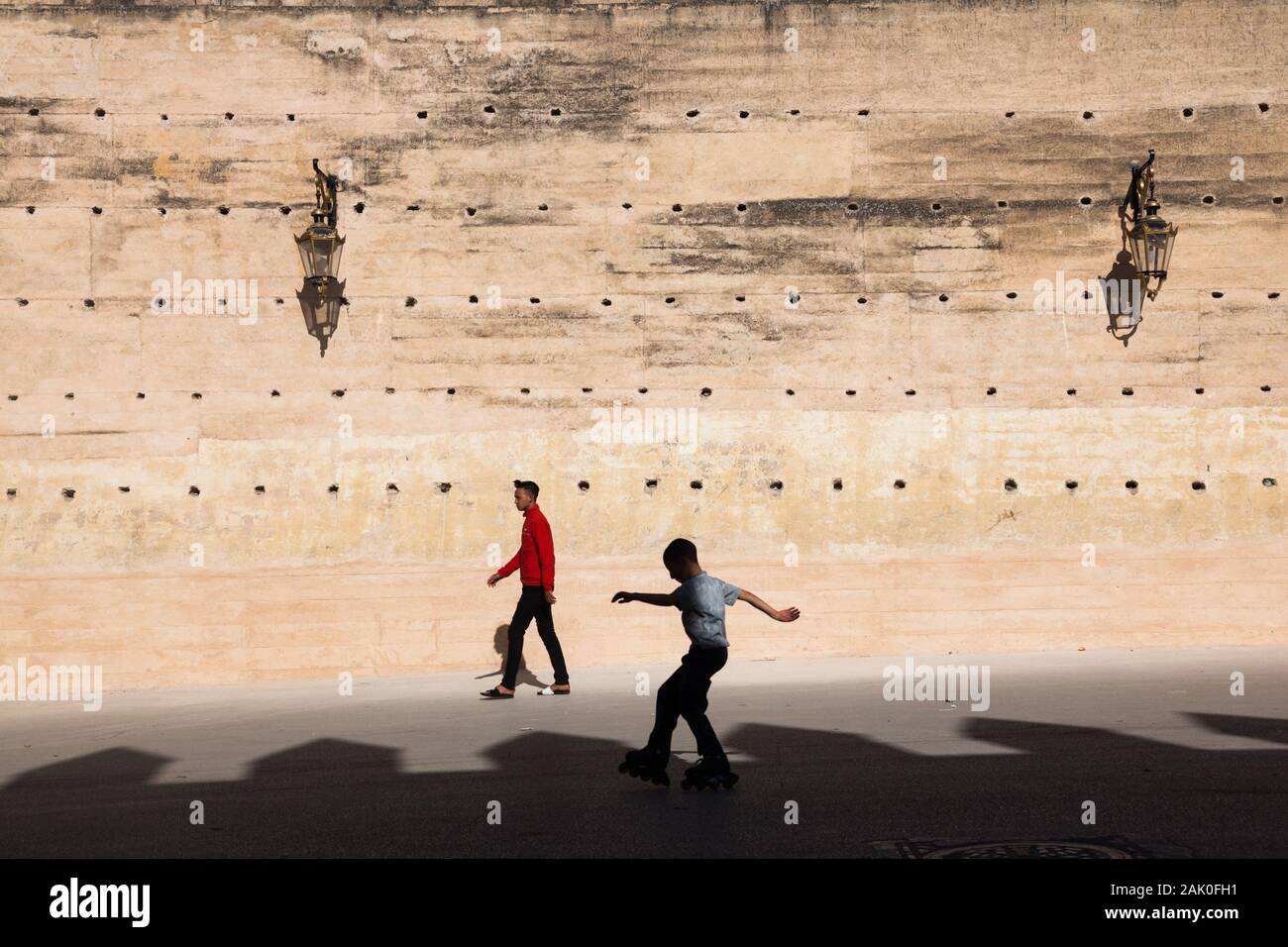 Un peatón, un chico en patines y la tierra apisonada de las murallas de la ciudad de Fez (fez) con visible la sombra de la pared opuesta, Marruecos Foto de stock