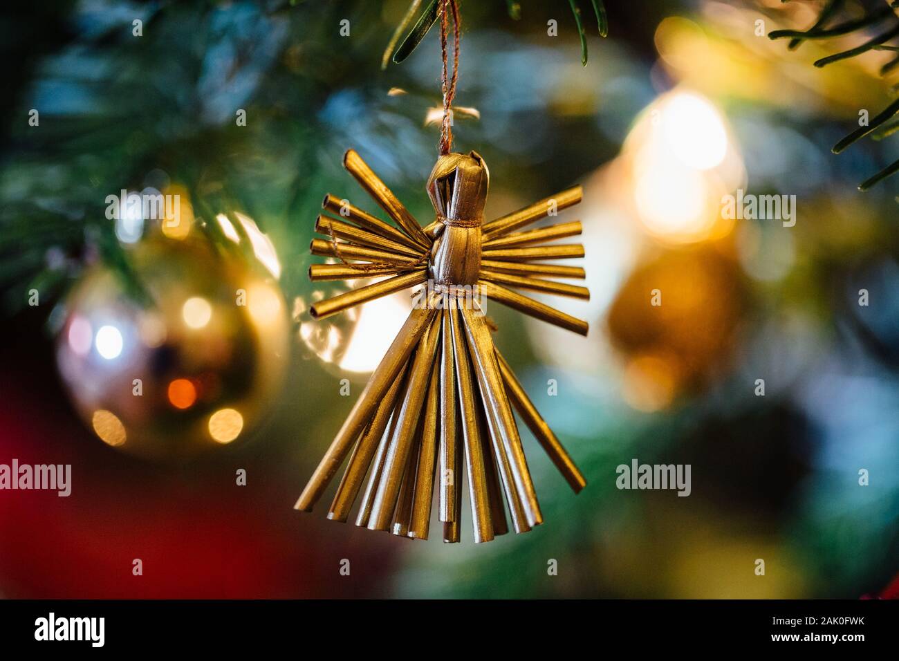Ángel de paja contra fuera de foco iluminado árbol de navidad. Foto de stock