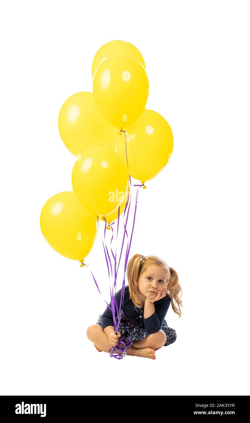 Retrato de una niña de 3 año de edad caucásico sentado y con globos de colores. aburrido expresión. aislado en blanco. Foto de stock