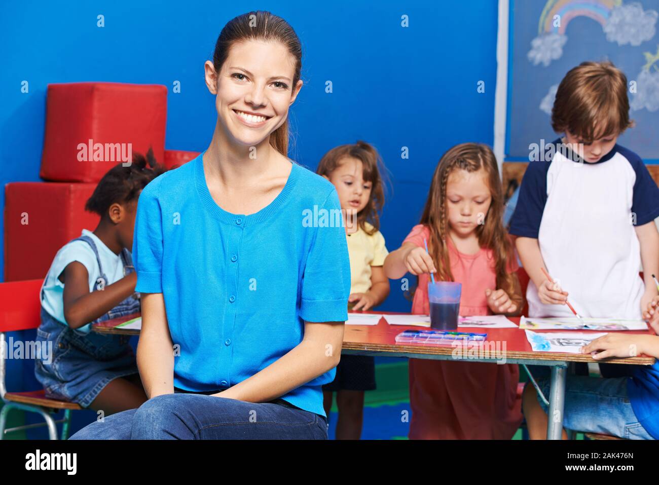 Educador sonriente delante del grupo de niños mientras la pintura en kindergarten. Foto de stock