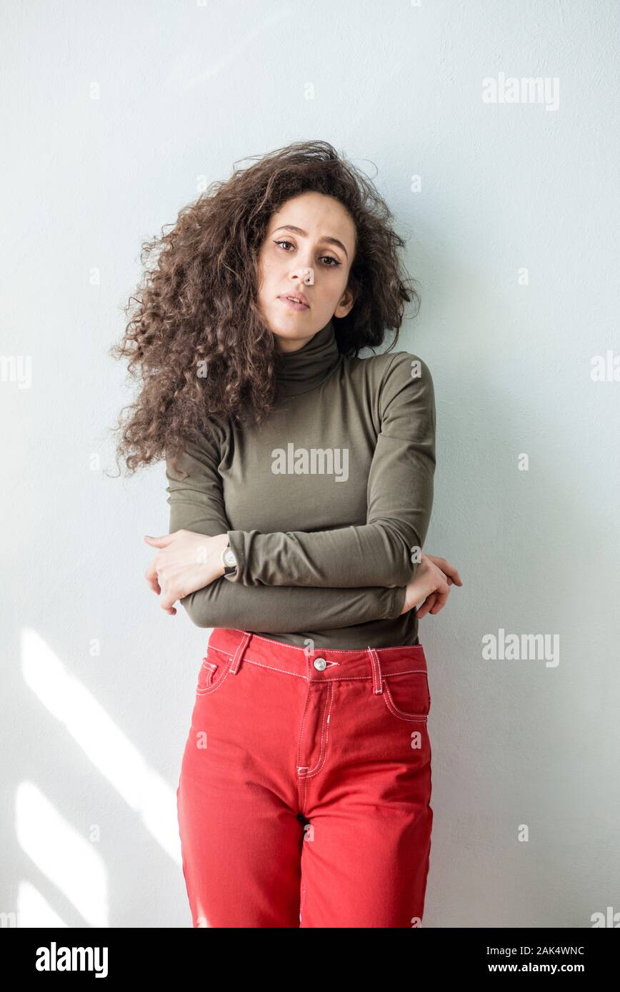 Mujer joven con el cabello rizado en vestimenta casual contra la pared blanca liberado Foto de stock