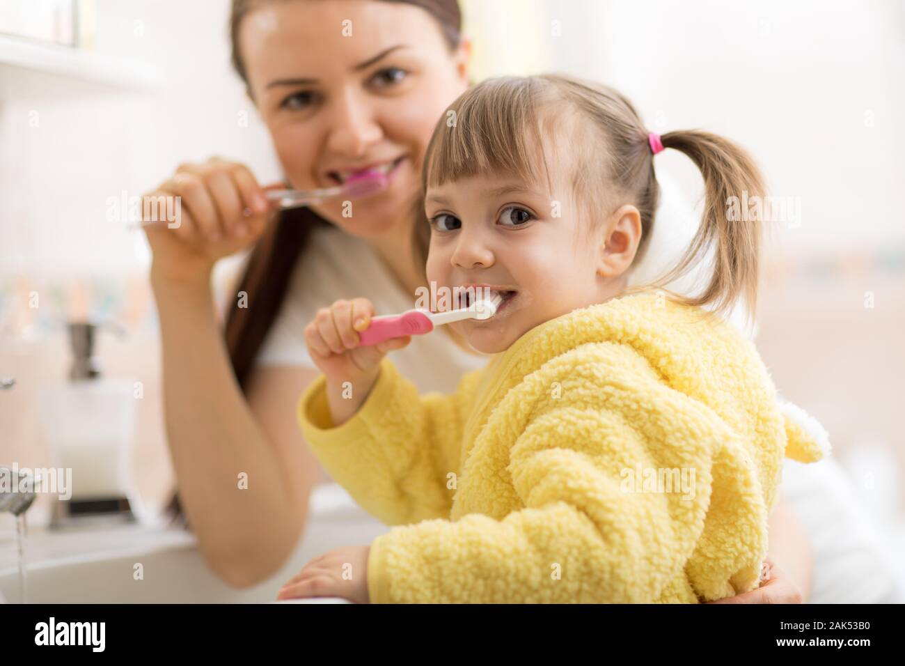 Niño sonriente chica con su mamá el cepillado y la limpieza de los dientes en el baño. Foto de stock