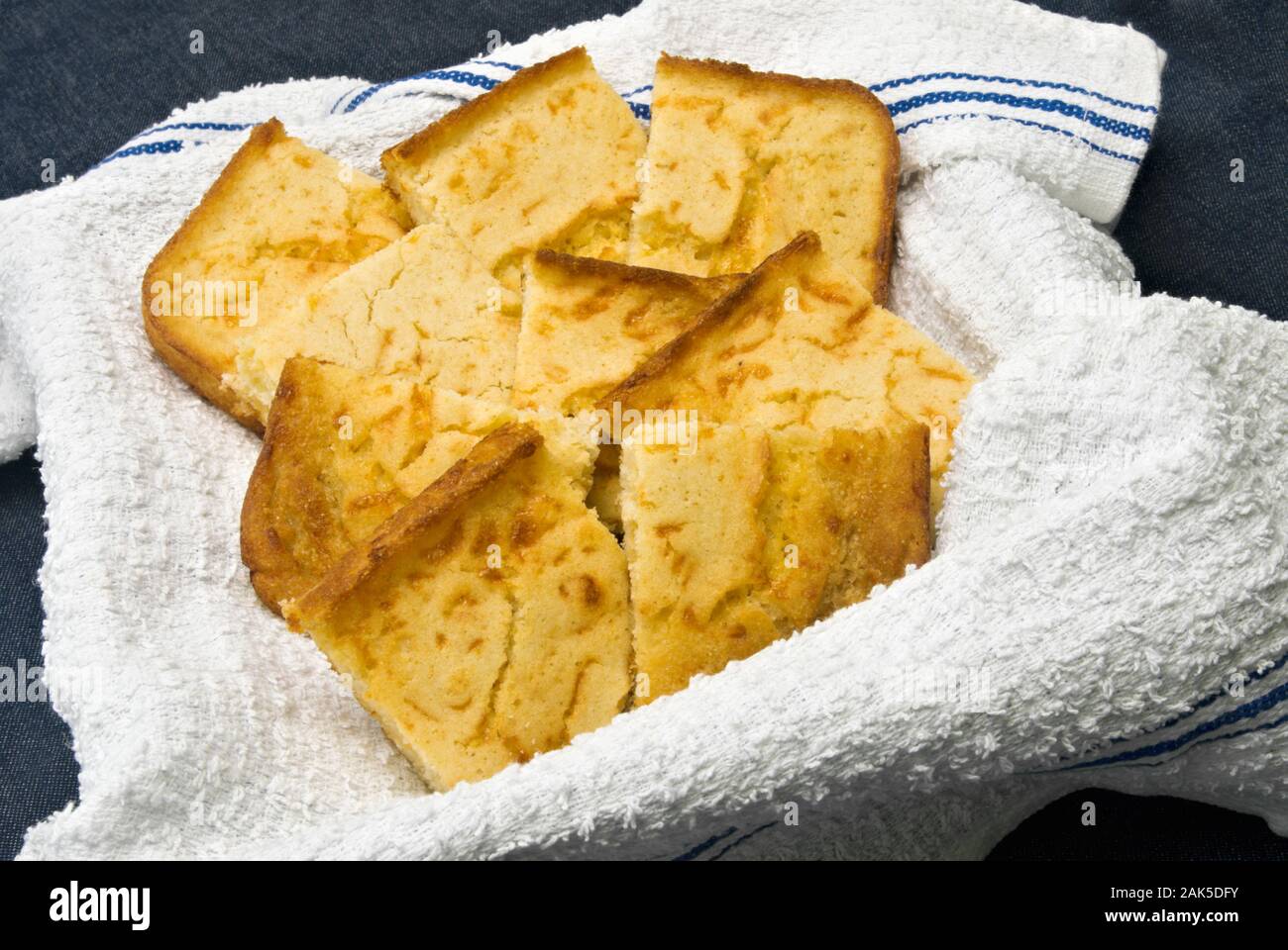 Pan de Maíz amarillo casero con costra crujiente servido sobre una toalla de cocina blanco nuevo dentro de una canasta. El fondo es azul tejido. Foto de stock