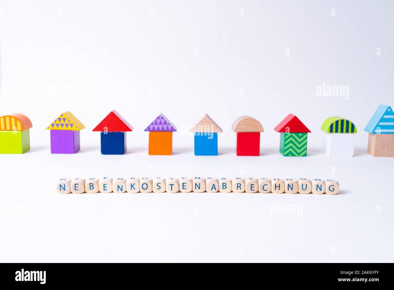 Cubos con cartas diciendo 'Nebenkostenabrechnung', la palabra alemana para costos adicionales factura en frente de una fila de casas construidas de juguete Juguetes coloridos Foto de stock