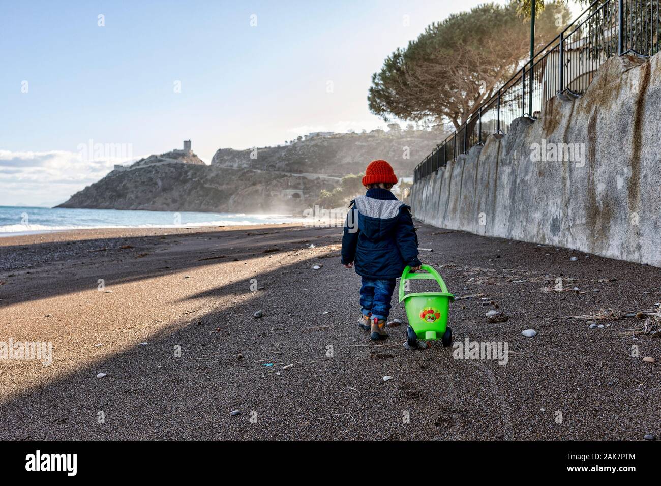 Little Baby caminando por una playa tirando de un carro de plástico Foto de stock