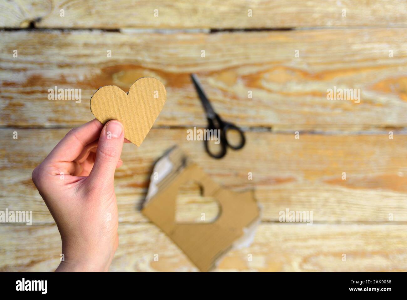 Corazón de cartón en manos de la mujer. Tarjeta sostenible para celebrar el Día de San Valentín. El concepto de reutilización Foto de stock