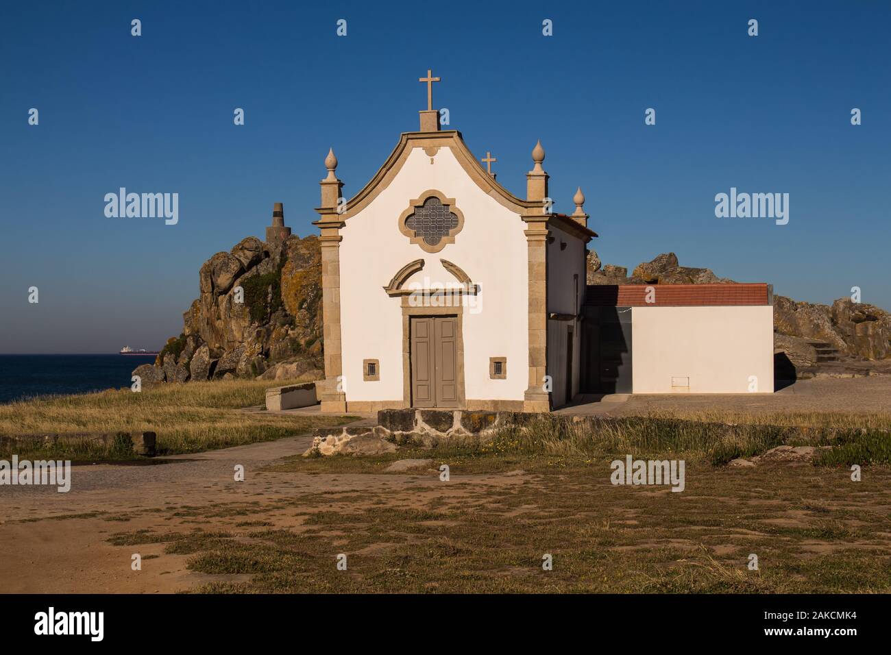 Pequeña capilla blanca construido en estilo tradicional portugués, en la costa del océano Atlántico, junto a una roca. Cielo azul brillante. Porto, Portugal. Foto de stock