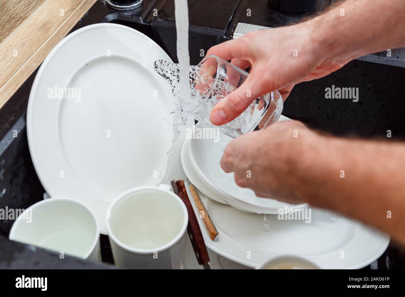 Lavar los platos - el hombre de manos en guantes de vidrio lavado bajo el grifo de agua en el fregadero. Foto de stock