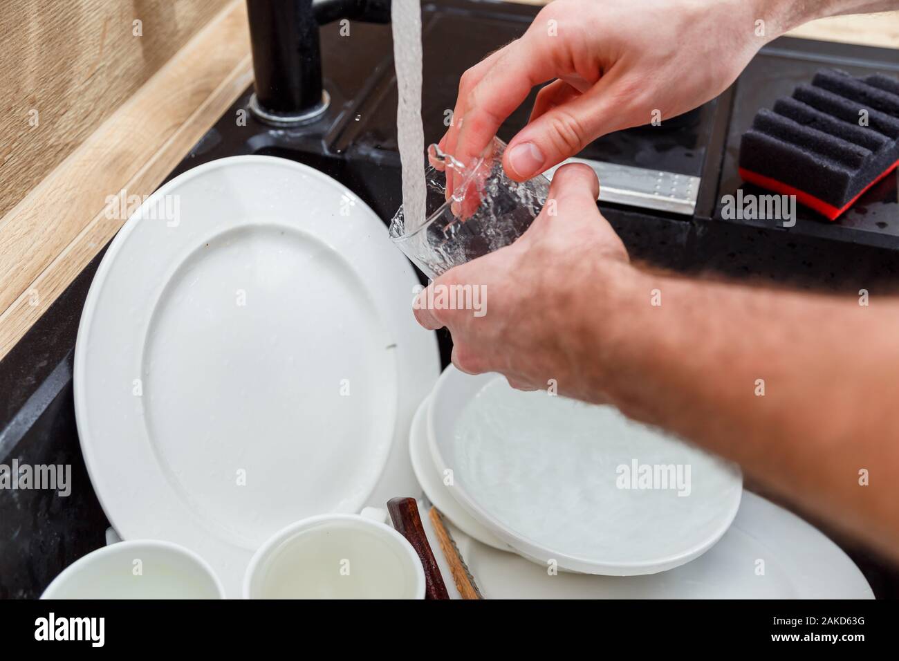 Lavar los platos - el hombre de manos en guantes de vidrio lavado bajo el grifo de agua en el fregadero. Foto de stock