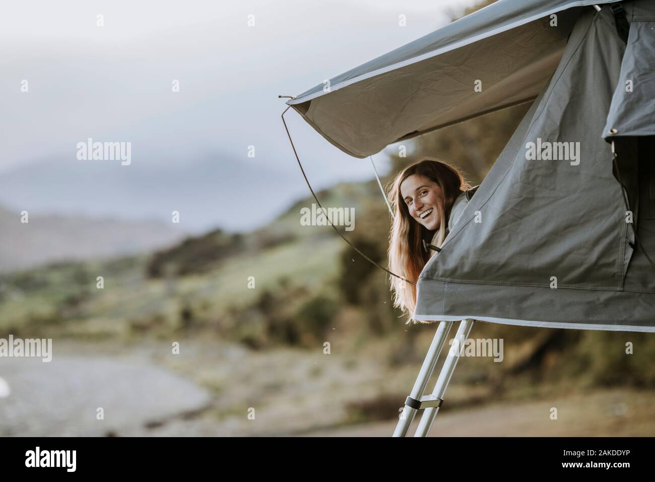 Una joven mujer sonriente se pega la cabeza de una tienda de campaña en Nueva Zelanda. Foto de stock