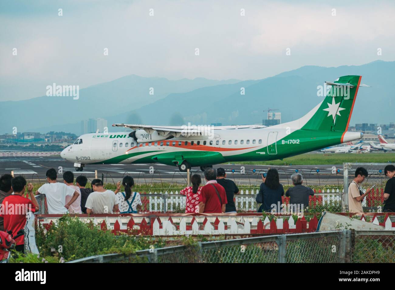 Un avión UNI Air se alinea en la pista del aeropuerto de Songshan, mientras que una multitud de personas observan desde fuera de la valla Foto de stock