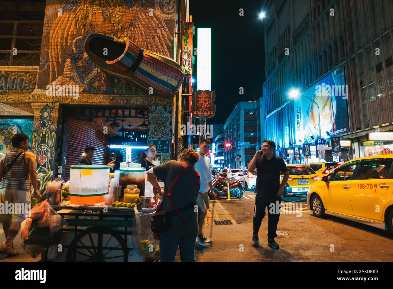 Un vendedor de la calle vende refrescos en una esquina de la calle, un hombre habla por teléfono y un clog gigante está montado en la pared de una tienda de zapatos Foto de stock