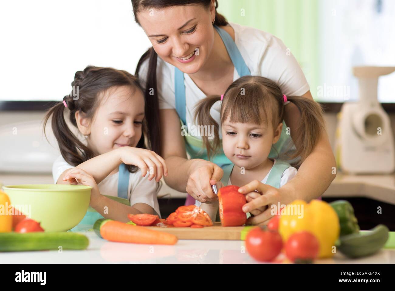 Madre de familia con hijos hijas picar las verduras en la cocina de hogar Foto de stock