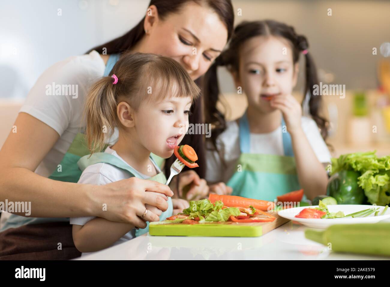 Madre de familia con hijos hijas picar las verduras en la cocina de hogar Foto de stock