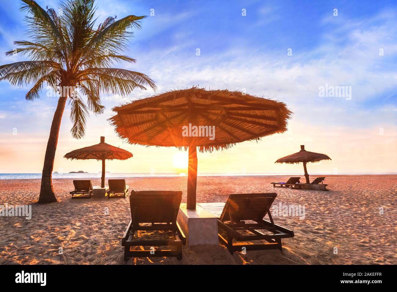 Paisaje de playa tropical al atardecer, vacaciones de verano en el paraíso lujoso hotel resort costero, palmeras, tumbonas tumbonas y una sombrilla en la Foto de stock