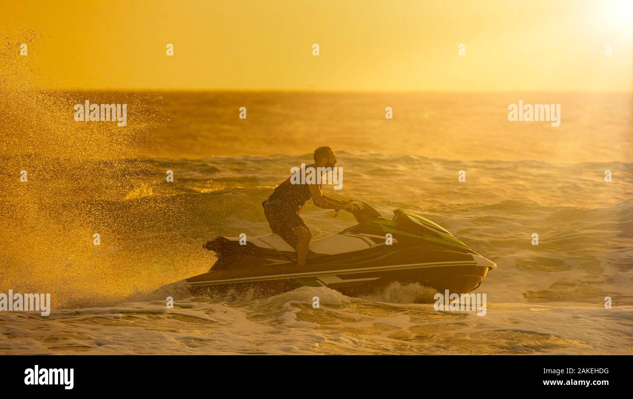 Silueta del hombre montando una moto de agua rápida a través de las olas en el amanecer Foto de stock