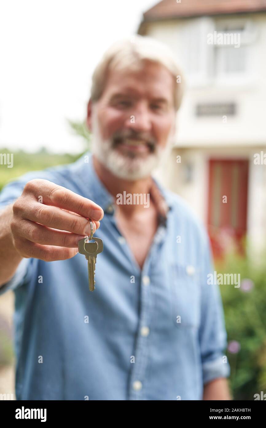Retrato de hombre maduro, de pie en el jardín de enfrente de la casa de sus sueños en el campo sosteniendo llaves Foto de stock