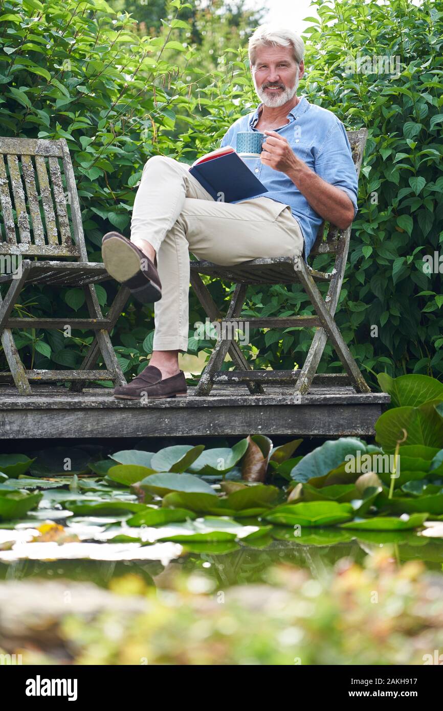 Retrato De Hombre Maduro Relajándose En El Libro De Lectura Del Jardín En Jetty By Lake Foto de stock