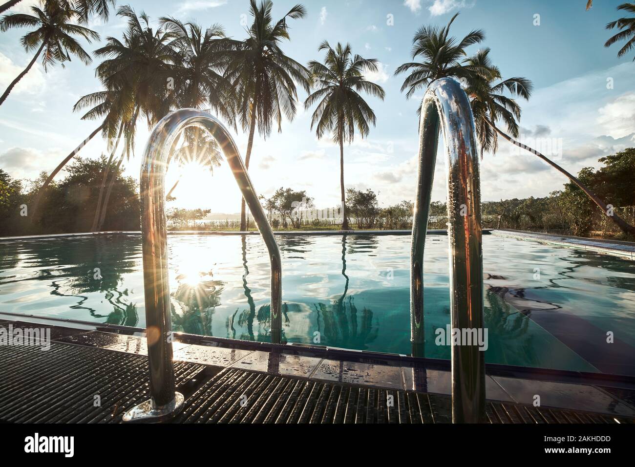 Relajación en lugar turístico. Piscina en medio de palmeras de coco contra la laguna al atardecer. Foto de stock