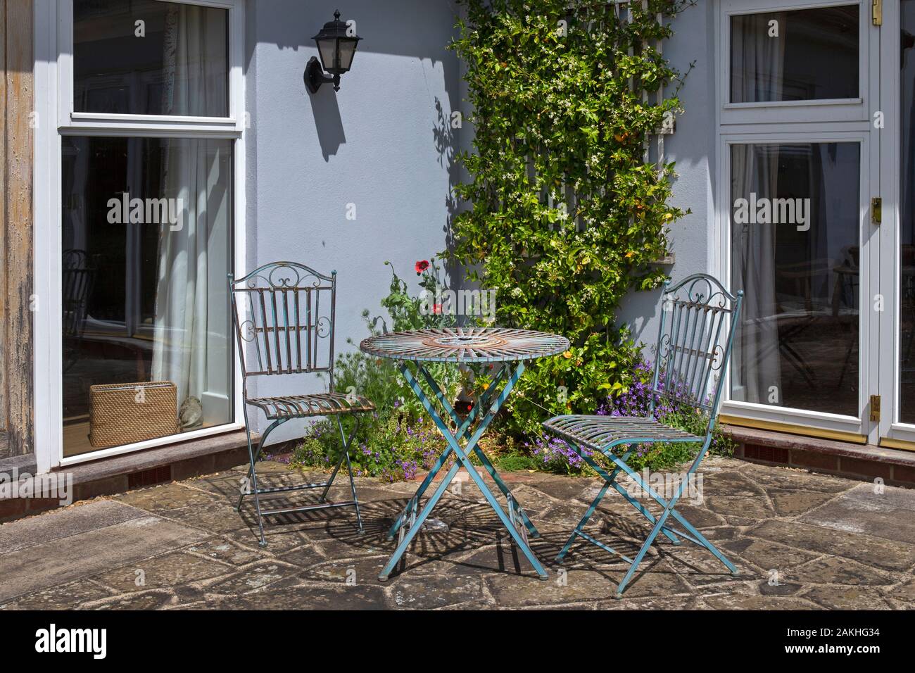 Jardín de metal con mesas y sillas en patio de piedra en jardín inglés de verano Foto de stock