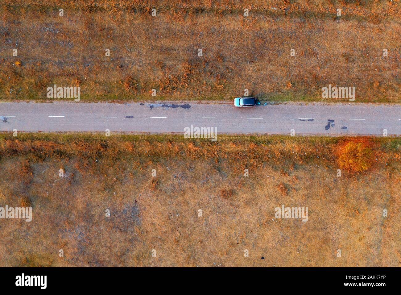 La mujer y el coche en carretera a través de grassy eriales, vista aérea directamente encima de drone POV Foto de stock