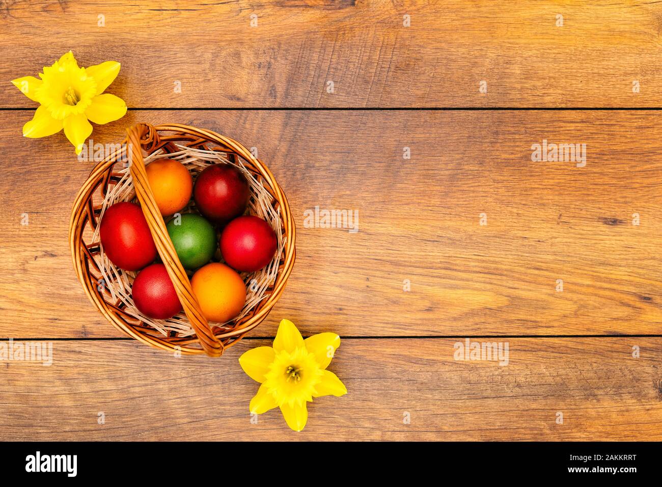 Siete coloridos huevos de Pascua en colores pastel en la cesta y amarillo dos Narcisos en vintage recuperadas de fondo de roble, vista superior Foto de stock