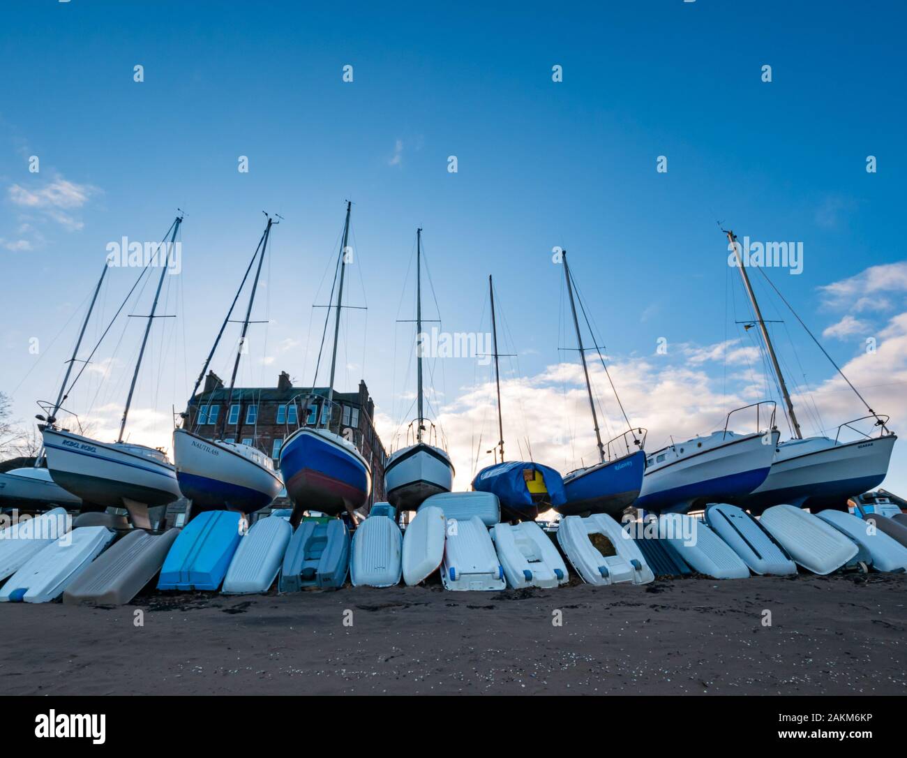 Barcos de vela fuera del agua para el invierno con botes a remo, Fisherrow Harbor, Musselburgh, Scotland, Reino Unido Foto de stock