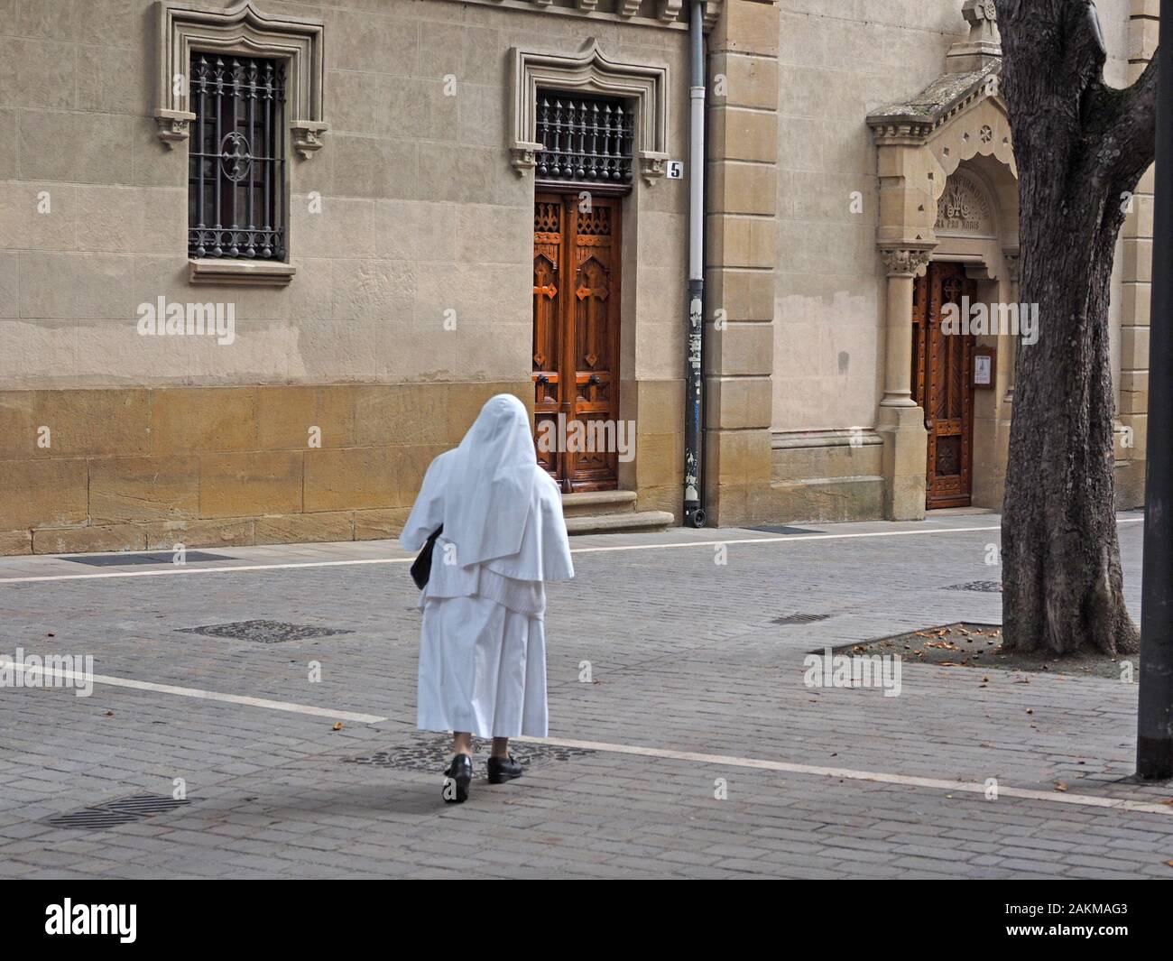Una monja en solitario simple hábito blanco (túnica y escapulario) cruza una plaza pavimentada hacia un en Pamplona, Fotografía de stock - Alamy