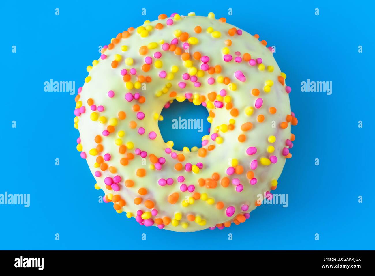 Donut amarillo vidriado con un agujero sobre fondo azul. Concepto de alimentos calóricos poco saludables. Humor divertido Foto de stock