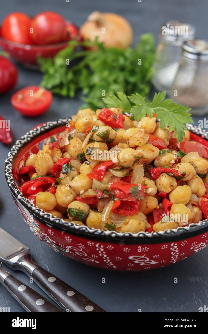 Garbanzos con guarnición de pimiento y tomate, un plato vegetariano ricos en proteína, que se encuentra en una placa contra un fondo oscuro, orientación vertical Foto de stock