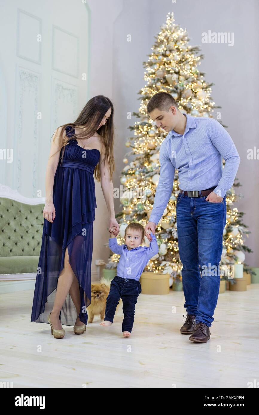 Feliz Pareja Joven Y Su Hijo Bebe Cerca Del Arbol De Navidad En Casa Mama Y Papa Agarrando Las Manos De Nino Pequeno Y Ayudandole A Hacer Los Primeros Pasos Fotografia De Feliz Pareja Joven Y Su Hijo Bebe Cerca Del Arbol De Navidad En Casa Mama Y Papa Agarrando Las Manos De Nino Pequeno Y Ayudandole A Hacer Los Primeros Pasos Fotografia De