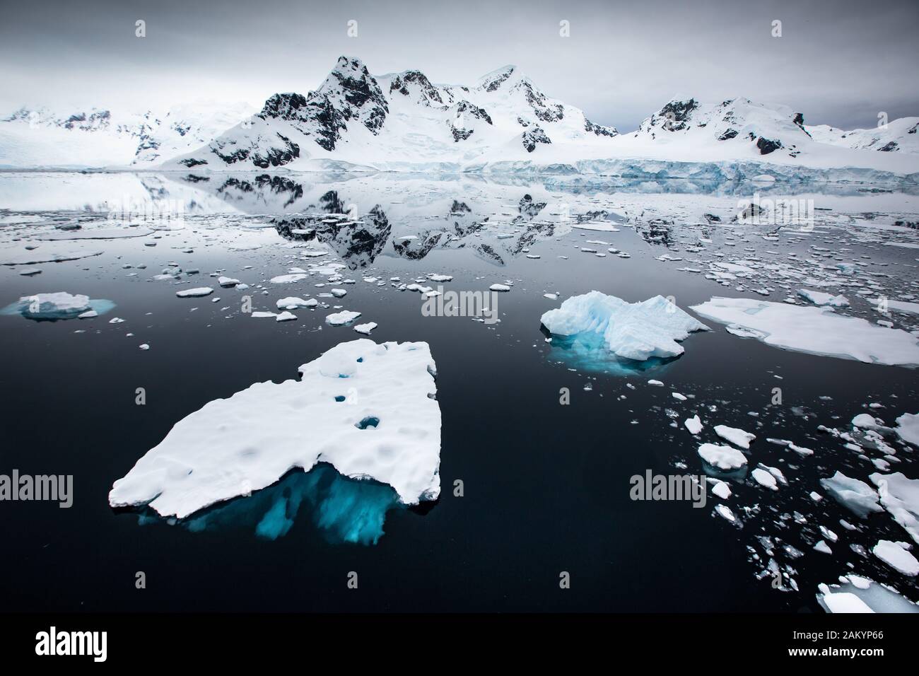Glaciar hielo, hielo de ladrillo, icebergs frente a las montañas y glaciares de la bahía del Paraíso con reflejos oceánicos sobreatmosféricos, Antártida Foto de stock