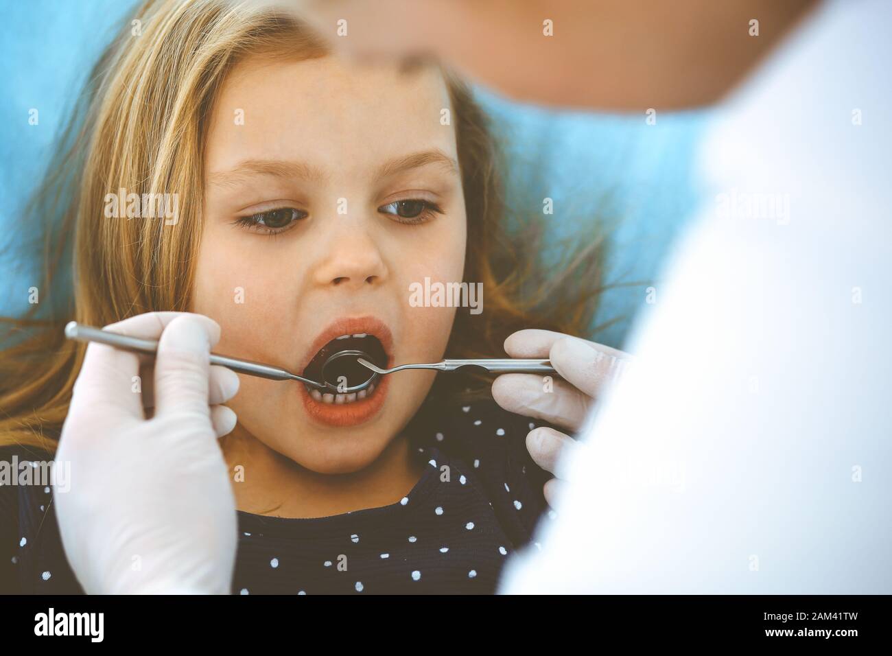 Hijita sentado en el sillón dental con la boca abierta durante la revisión oral al médico. Visitando la oficina de dentista. Concepto de medicina. Foto de tonos Foto de stock
