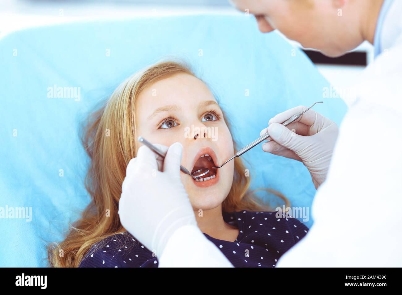 Hijita sentado en el sillón dental con la boca abierta durante la revisión oral al médico. Visitando la oficina de dentista. Concepto de medicina. Foto de tonos Foto de stock