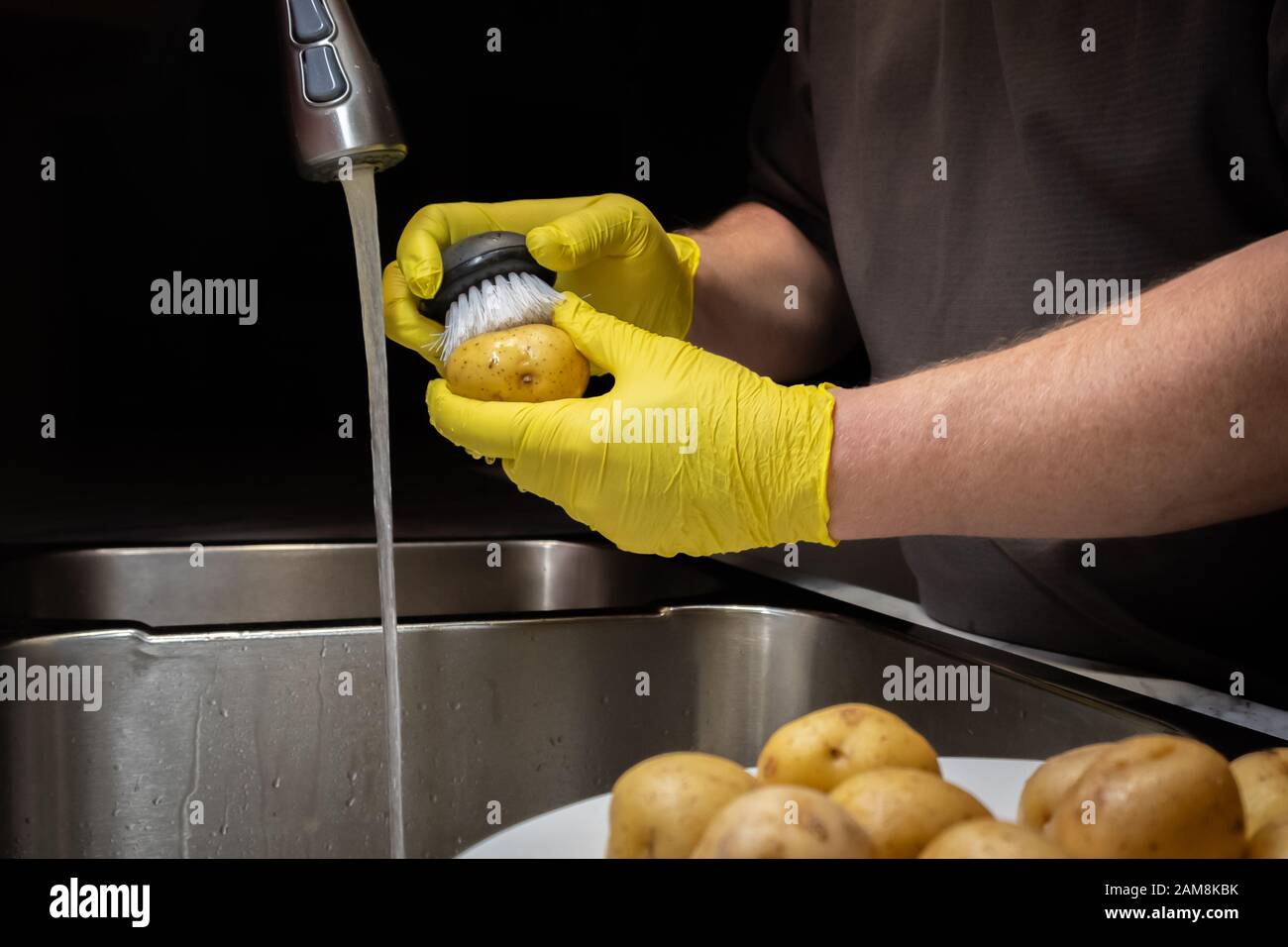 Lavar y enjuagar las patatas en preparación para cocinar. Modelo con guantes  de goma desechables amarillos Fotografía de stock - Alamy