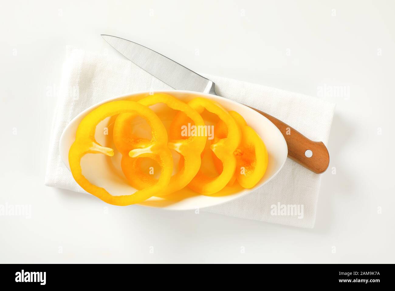 Pimentón amarillo en un Bol blanco y cuchillo de cocina al lado Foto de stock